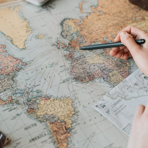 Hands marking destinations on a world map surrounded by travel essentials like passport and camera.